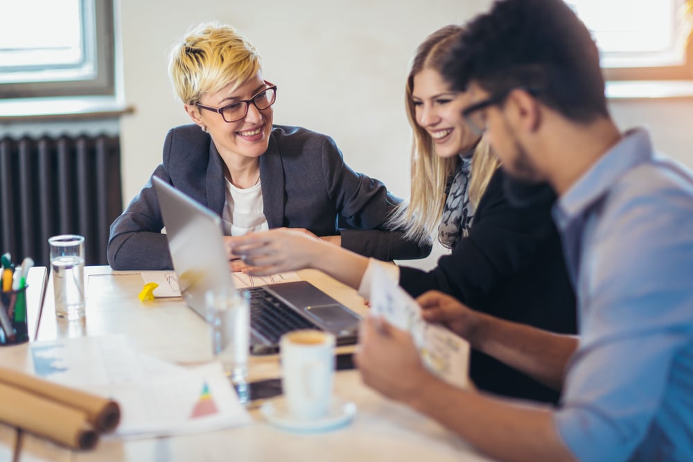 Three workers talking and smiling, looking at laptop