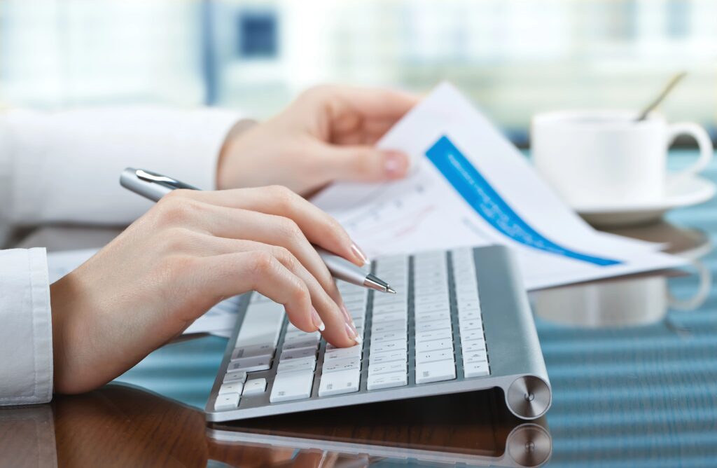 One hand typing on keyboard, the other holding up paper with data